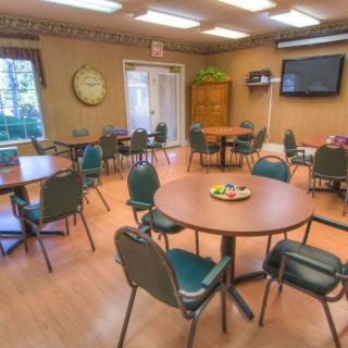 A well-lit meeting room with round tables, chairs, and a wall-mounted television.