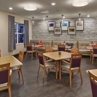 A modern restaurant dining area with tables and chairs, decorated with wall art and illuminated by stylish lighting fixtures.