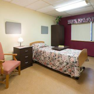 A simple, well-organized bedroom with a bed, chair, and a small dresser next to a window with curtains.