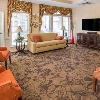 A spacious living room featuring a sofa, ornate patterned carpet, and a large television.