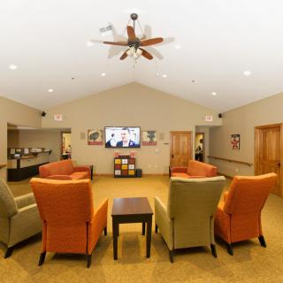 A cozy living room with colorful chairs arranged around a television and a ceiling fan.
