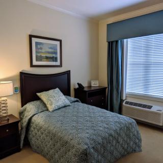 A neatly arranged bedroom with a single bed, nightstand, and large window with curtains.