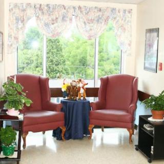 A cozy seating area with two red armchairs and a small table by a large window, adorned with plants.