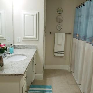 A neat and organized bathroom featuring a marble countertop, mirror, and blue-themed decor.
