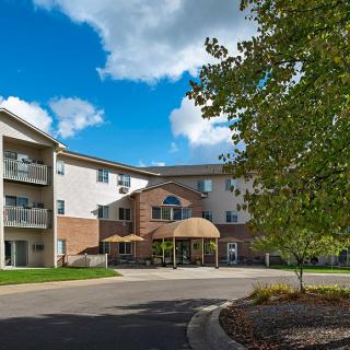 A modern residential apartment building with a driveway and surrounding trees under a clear blue sky.