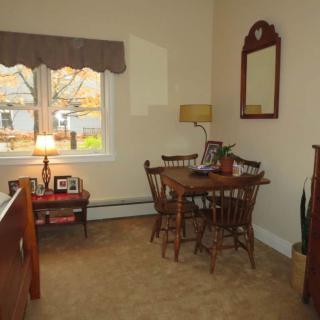 A cozy dining room with a wooden table and chairs, a mirror on the wall, and a lamp by the window.
