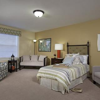 A cozy bedroom interior with a bed, sofa, lamps, and carpet.