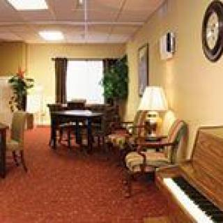 A cozy living room with a piano, various chairs and tables, and warm lighting.