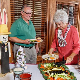 An elderly couple enjoys a buffet-style dinner at home, surrounded by festive decorations.