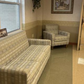 A cozy waiting room with a plaid sofa and armchair, decorated with wall art and a picture frame.