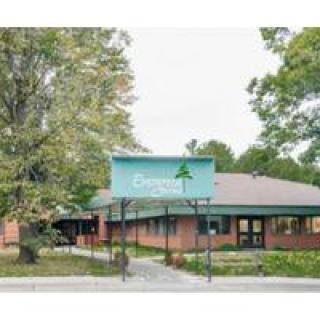 A building with a green sign surrounded by trees, featuring an entrance area.