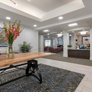 A modern lobby featuring a wooden table with floral arrangements and a reception area in the background.