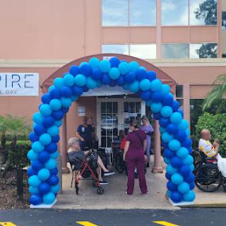 A colorful blue balloon arch welcoming visitors to a facility entrance, with people gathered outside.