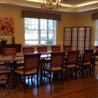 Elegant dining room with a long table and chairs, featuring a chandelier and large windows.