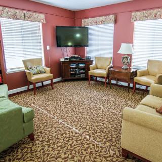 A cozy living room with sofas and armchairs arranged around a television, featuring a patterned carpet and warm color tones.