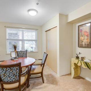 A cozy dining area with a round table and four chairs, featuring artwork on the wall and natural light from the window.