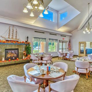 A cozy dining area featuring a fireplace, skylight, and decorative ship model, with neatly arranged tables and chairs.
