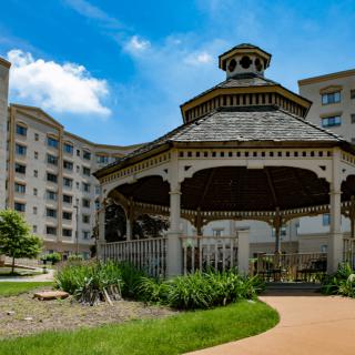 A gazebo in a landscaped garden area surrounded by a multi-story building under a bright blue sky.