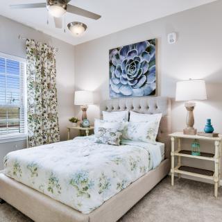 A cozy bedroom featuring a floral-themed bedspread, elegant artwork above the headboard, and stylish nightstands with lamps.