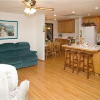 A cozy living room with an open floor plan connected to the kitchen, featuring a green couch, wooden bar stools, and a ceiling fan.