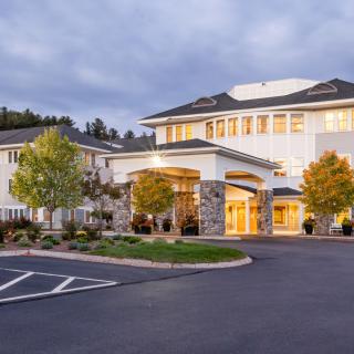 A large building with a welcoming entrance, surrounded by trees and set against an evening sky.