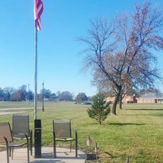 A peaceful patio setting with chairs near a flagpole and a tree on a sunny day.