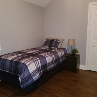 A simple bedroom with a single bed featuring plaid bedding, a nightstand, and a lamp.