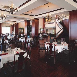An elegant restaurant interior with neatly arranged tables and chairs, illuminated by chandeliers.