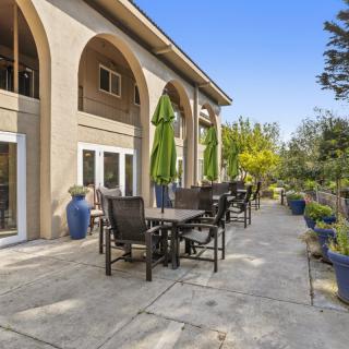 A spacious patio with tables, chairs, and umbrellas outside a building with arched architecture.