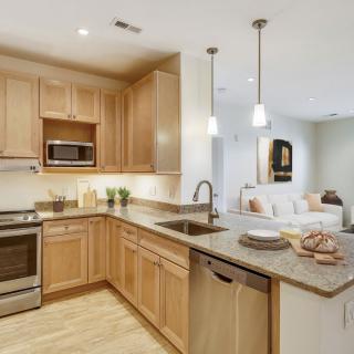 A modern kitchen with wood cabinets and stainless steel appliances in an open floor plan.