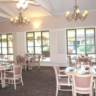A spacious dining room with neatly arranged tables and chairs, featuring elegant chandeliers and large windows.