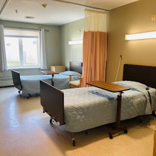 A view of a hospital patient room with two beds and natural light coming through the window.