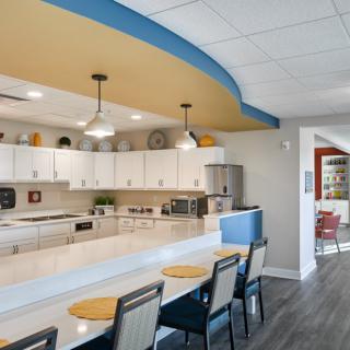 A modern kitchen with a long countertop and bar seating, featuring white cabinets and stylish pendant lights.