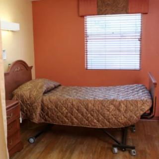 A simple bedroom with a single bed in a healthcare facility, featuring an orange accent wall and wooden flooring.