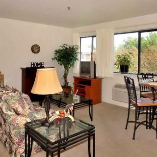 A cozy living room with a floral sofa, glass-top tables, and a dining area by the window.