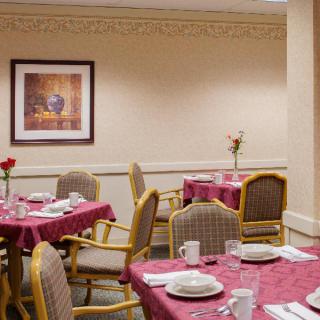 A neatly arranged dining area with tables covered in red tablecloths, set with white dishware and surrounded by cushioned chairs.