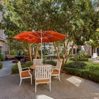 A peaceful outdoor seating area with a red umbrella and patio furniture surrounded by greenery.