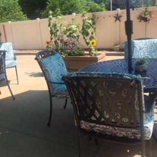A sunny patio with chairs and a table surrounded by greenery.