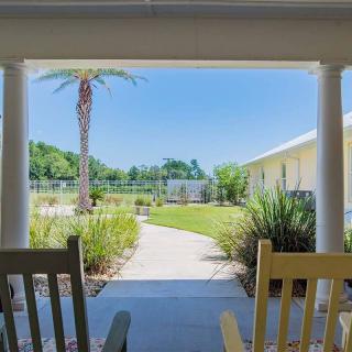 A peaceful outdoor patio with rocking chairs overlooks a garden and palm trees under a clear blue sky.