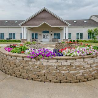 A well-maintained building entrance with a circular flower garden and stone wall.