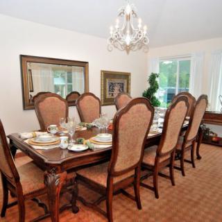 An elegant dining room with a large table, upholstered chairs, and a chandelier.