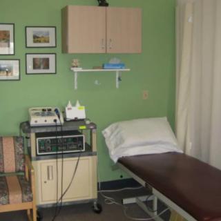A small doctor's office with an exam table, medical equipment, and wall decor.