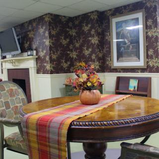 A cozy dining area featuring a wooden table with a colorful table runner and floral arrangement, set against patterned wallpaper.