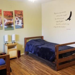 A cozy and minimalist bedroom with a single wooden bed, wall art depicting nature scenes, and a small bedside table.