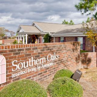 A brick sign for 'Southern Oaks' in front of a residential building with landscaped bushes and a cloudy sky.
