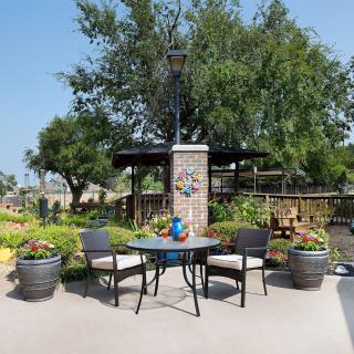 A cozy outdoor patio with a table and chairs surrounded by greenery and a lamp post.