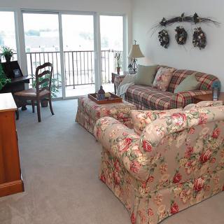 A cozy living room with floral-patterned furniture and a view of the balcony.