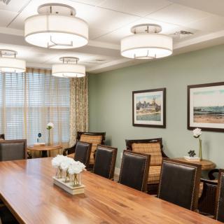 A well-lit conference room with a large wooden table and several chairs, decorated with framed art on the walls.