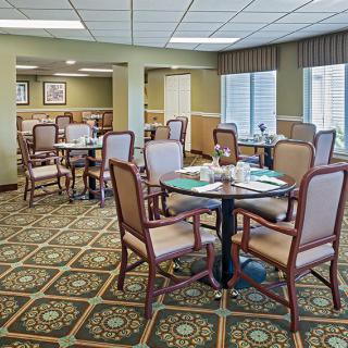 A spacious dining room with tables and chairs, featuring large windows and patterned carpet.