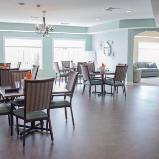 A modern and spacious dining room with multiple tables and chairs, well-lit by large windows.
